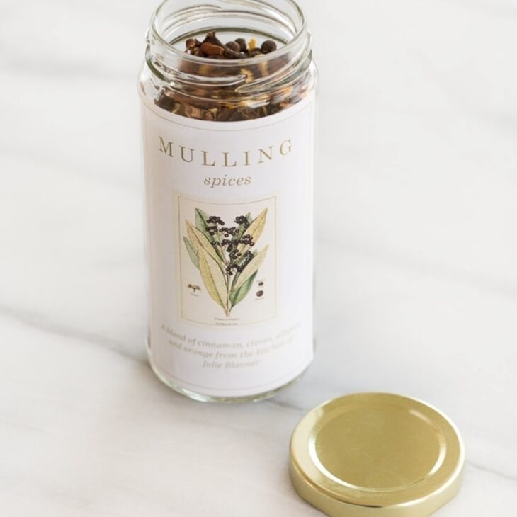 A bottle of mulling spices resting on a marble countertop, with a gold lid to the side.