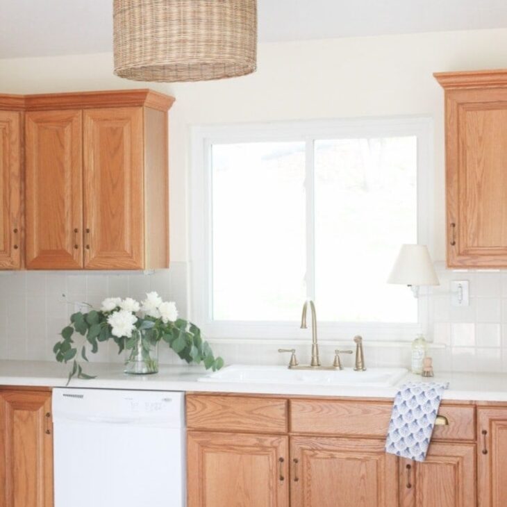 A white kitchen with oak kitchen cabinets and a coastal light fixture in the center