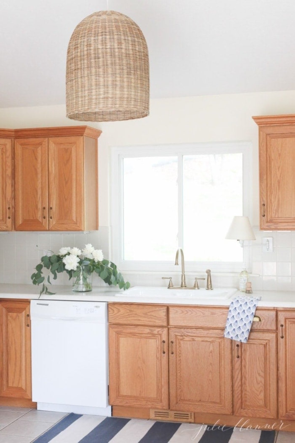 A white kitchen with oak kitchen cabinets and a coastal light fixture in the center