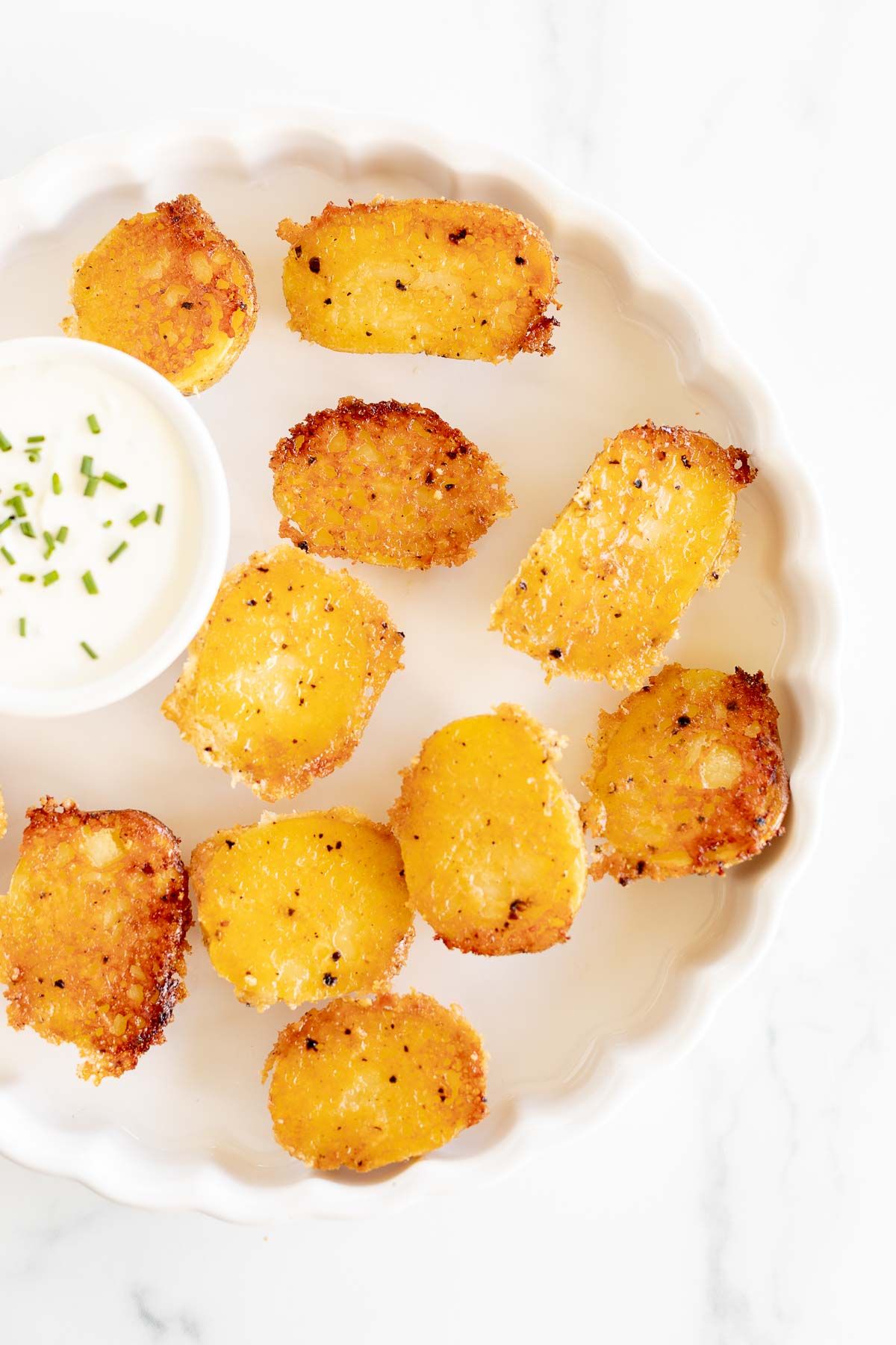 A white ruffled plate full of parmesan potatoes, with a small bowl of sour cream dip.