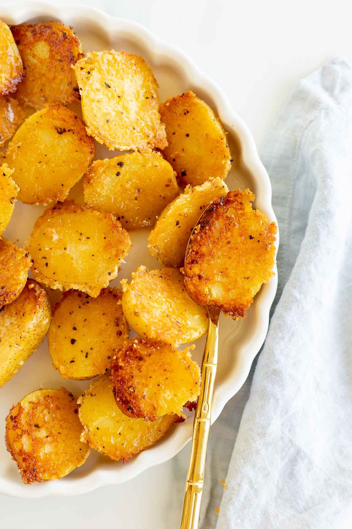 Parmesan roasted potatoes on a white plate, with a gold spoon