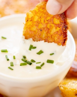 A hand dipping a Parmesan roasted potato into a white bowl of sour cream dip