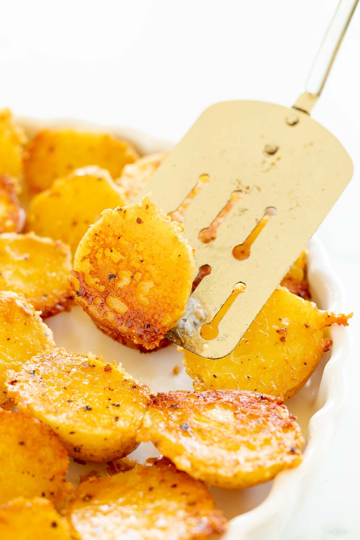 Parmesan roasted potatoes on a white plate, with a metal spatula