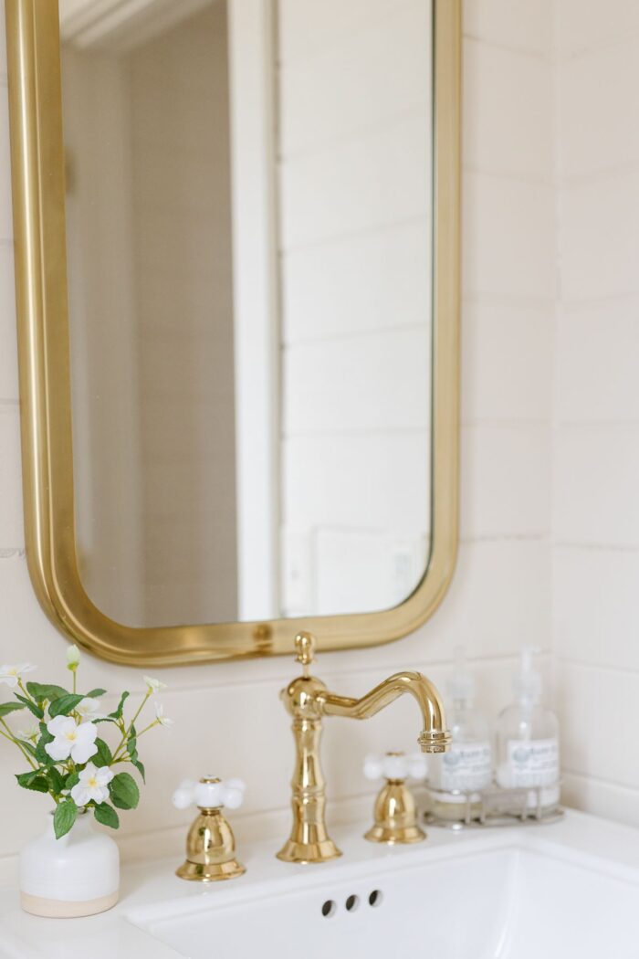 A powder room with a brass mirror and brass bathroom faucet