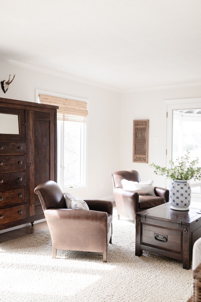 A family room with leather chairs, dark wood furniture and a natural looking rug from Wayfair