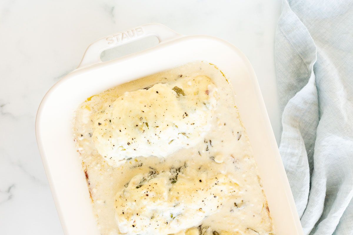 Baked chicken and spinach in a white casserole dish.