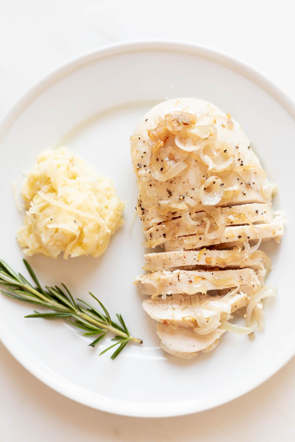 A white plate, topped with sliced garlic chicken with shallots, a scoop of mashed potatoes to the side.