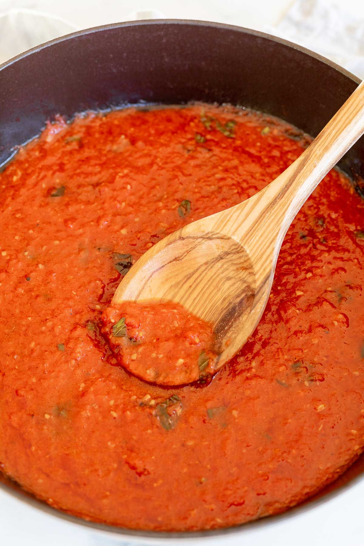 San Marzano tomato sauce in a cast iron pan, topped with chopped herbs and a wooden spoon