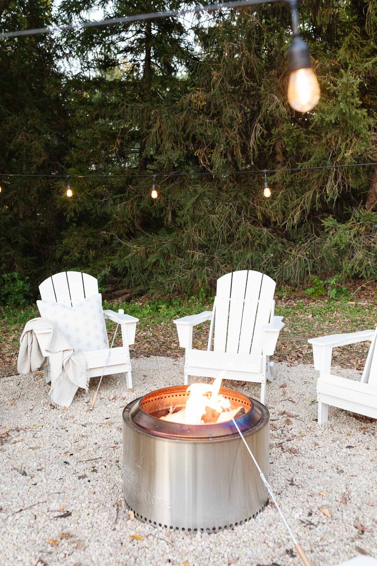 White Adirondack chairs, circling a Solo Stove on a DIY pea gravel fire pit patio.
