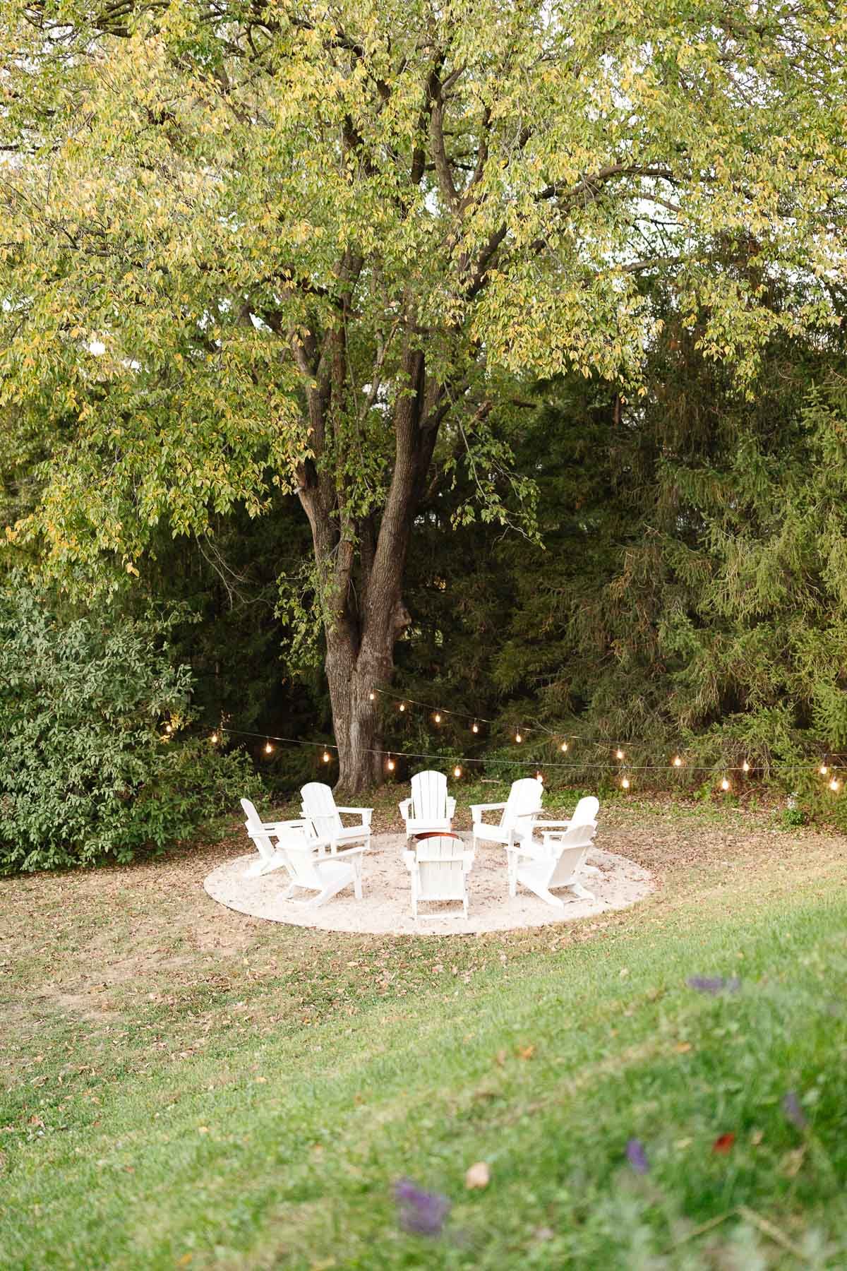 White Adirondack chairs, circling a Solo Stove on a DIY pea gravel fire pit patio.