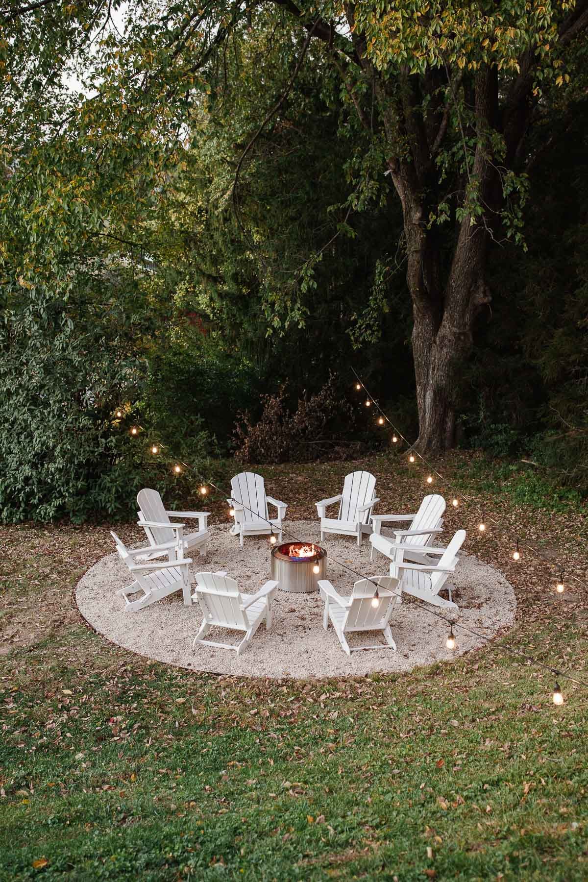 White Adirondack chairs, circling a Solo Stove on a DIY pea gravel fire pit patio.