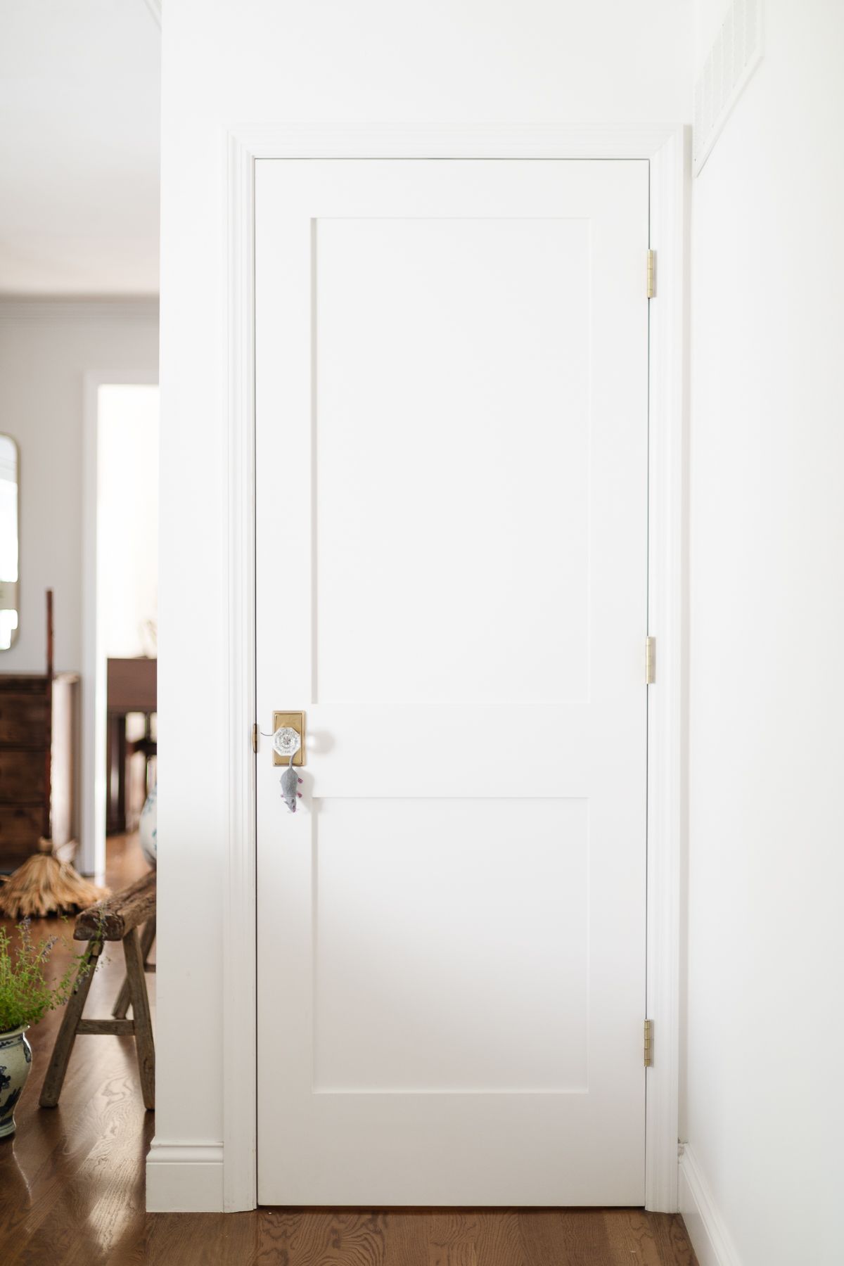 A fake plastic mouse hanging from the door handle of a white door in a white home.