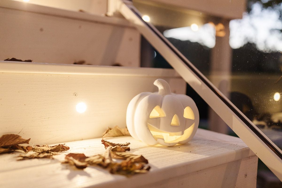 A white jack o lantern glowing on a white deck.