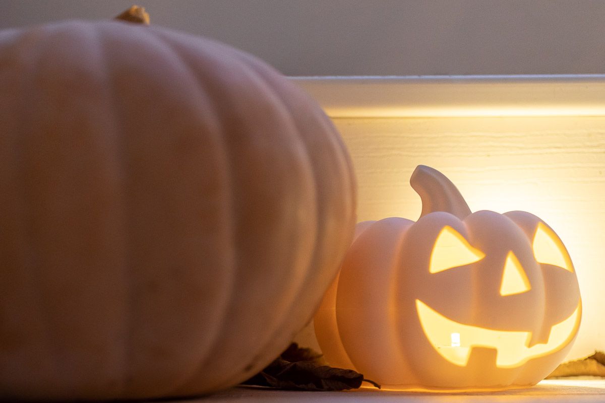 A peach heirloom pumpkin next to a glowing faux white jack o lantern on white deck steps.