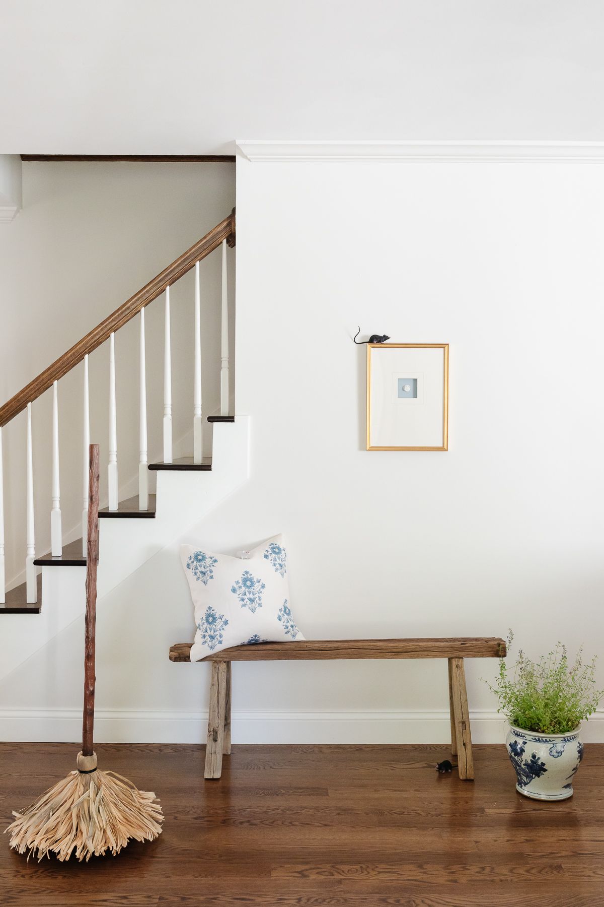 A witch's broom and fake mouse in a white entryway of a home with wood floors.