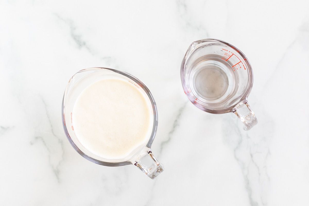 A white measuring cup of heavy whipping cream next to a glass measuring cup of water.