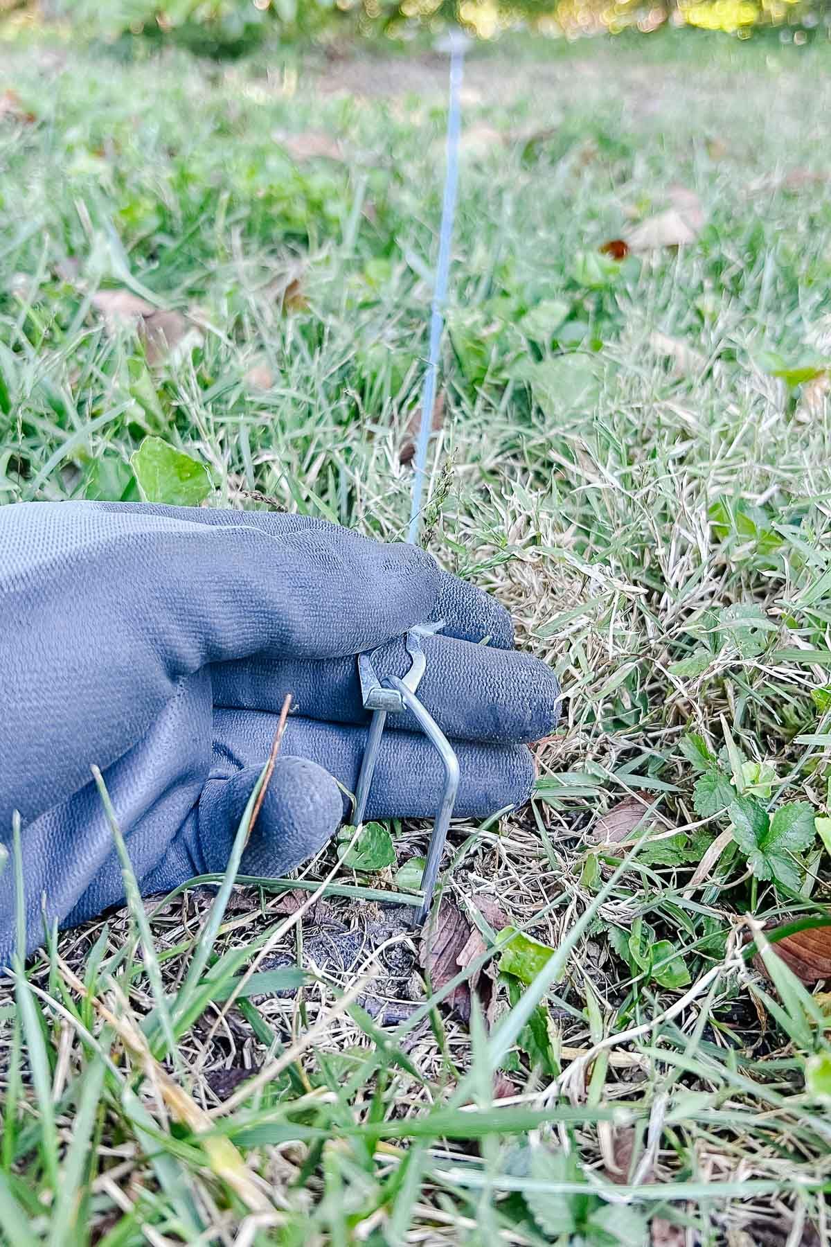 A gloved hand, holding a string to measure out a circle for a round fire pit patio