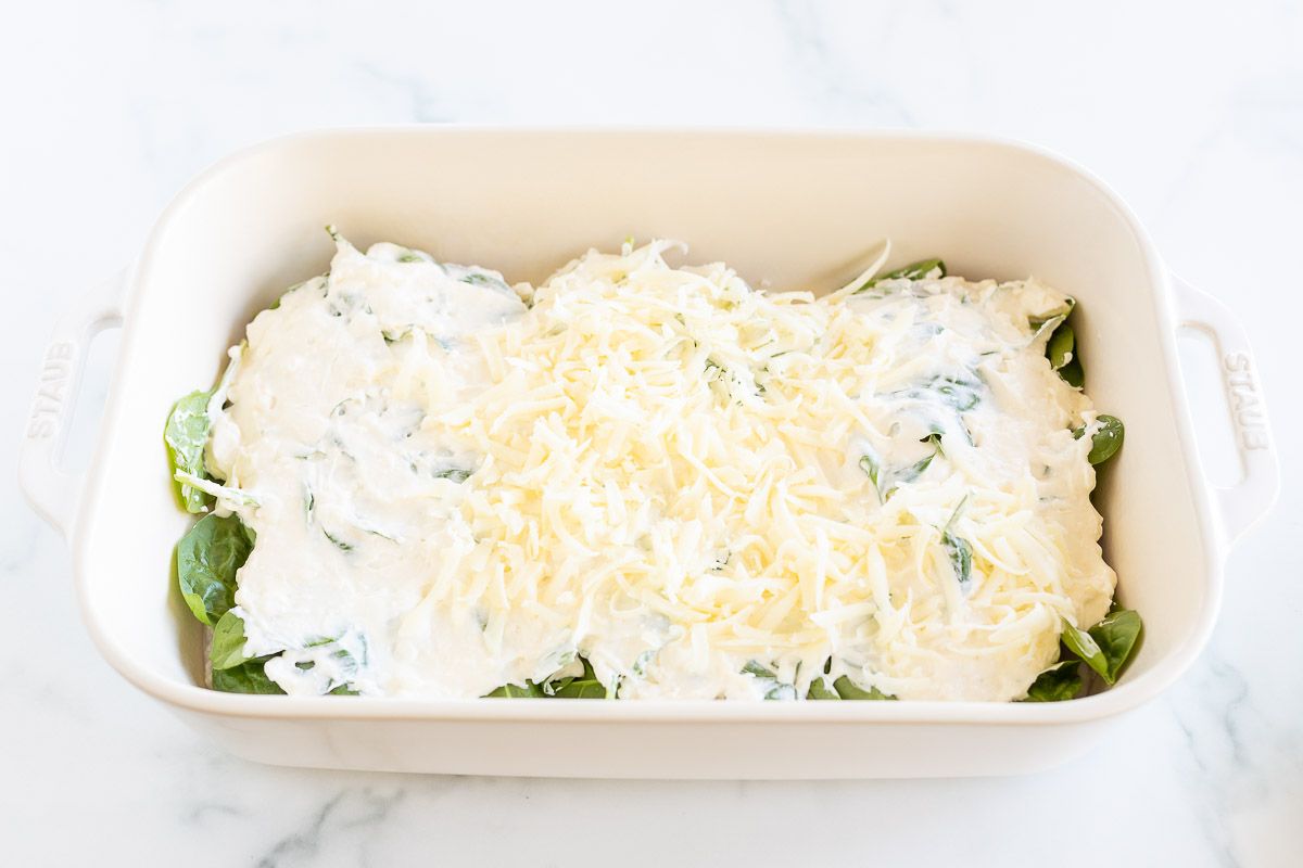 Chicken breasts covered with spinach and cheese in a white casserole dish.