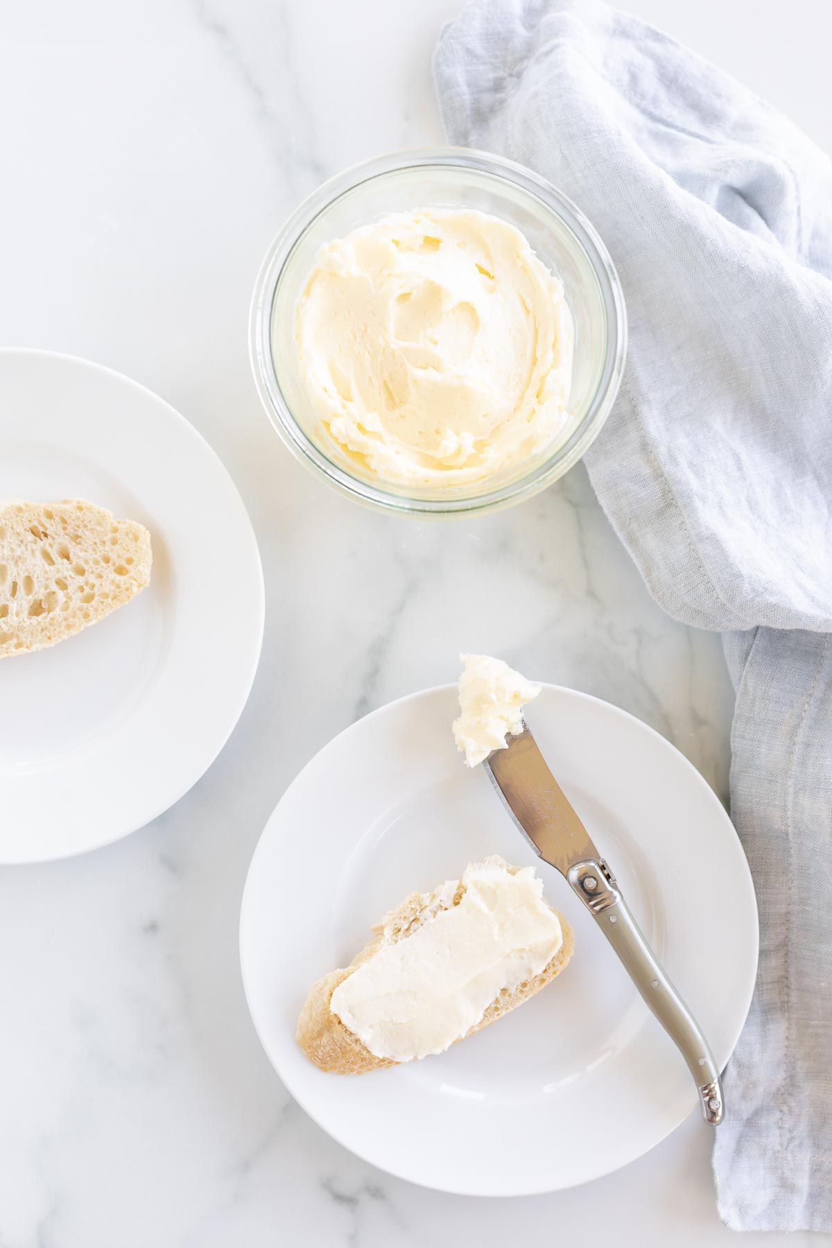 A small glass bowl of homemade butter, with a plate of sliced bread spread with butter nearby