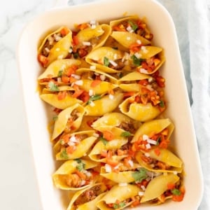 Taco stuffed shells in a white baking pan.