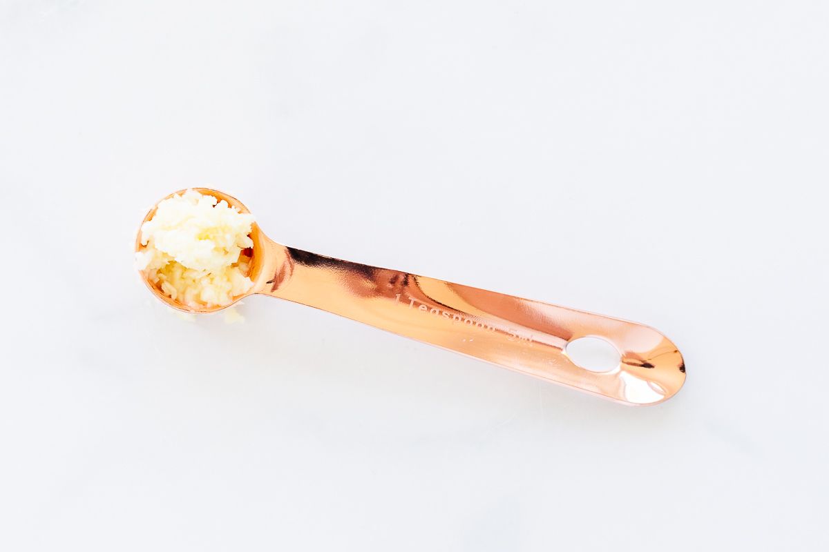 A copper teaspoon full of minced garlic on a marble surface