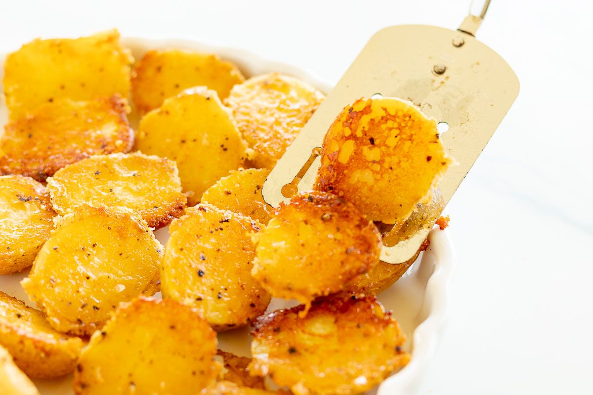 Parmesan roasted potatoes on a white plate, with a metal spatula