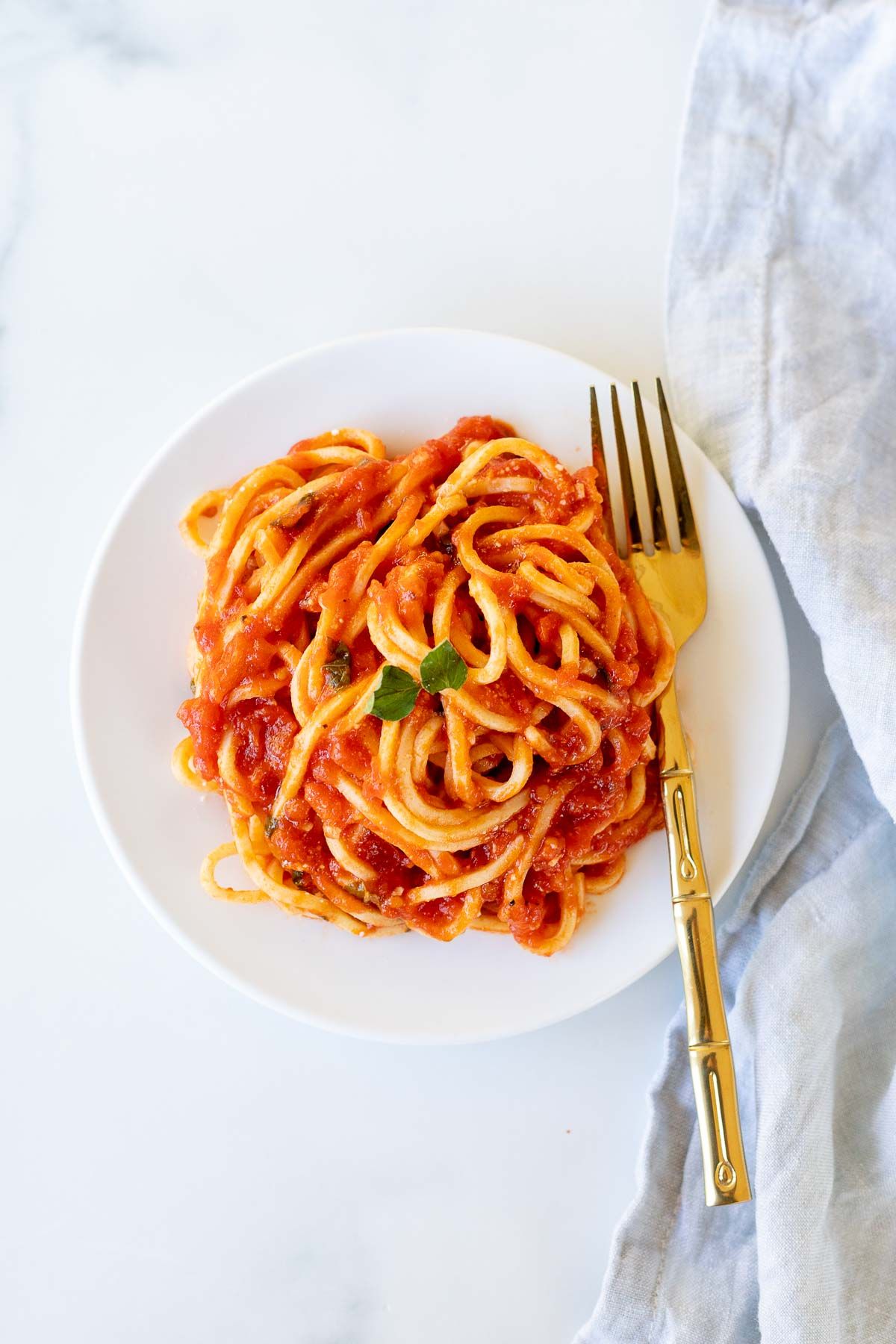 Spaghetti on a white plate, tossed in San Marzano tomato sauce, with a gold fork to the side. 