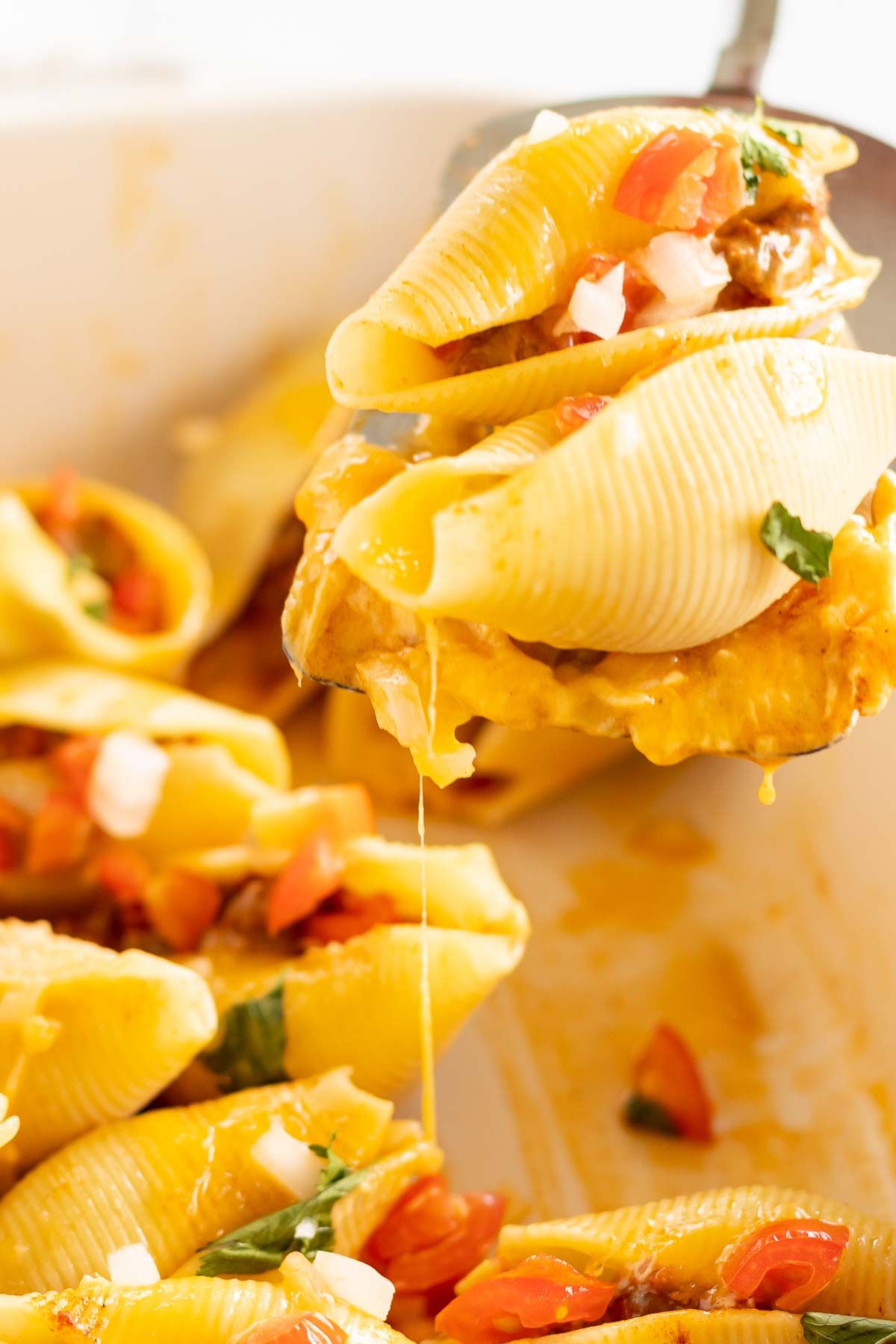 A close up of a spatula pulling a serving of taco stuffed shells out of a pan.