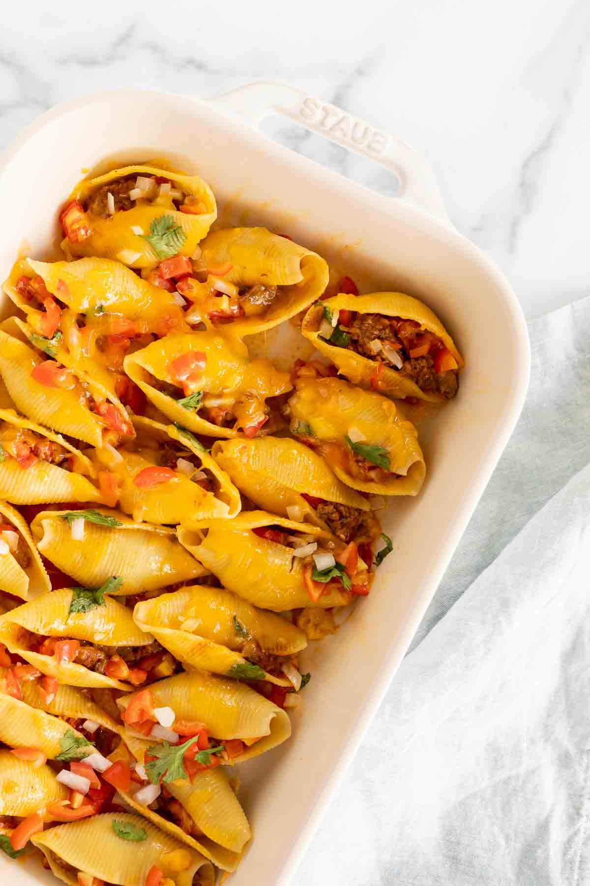 Taco filled shells in a white baking pan.