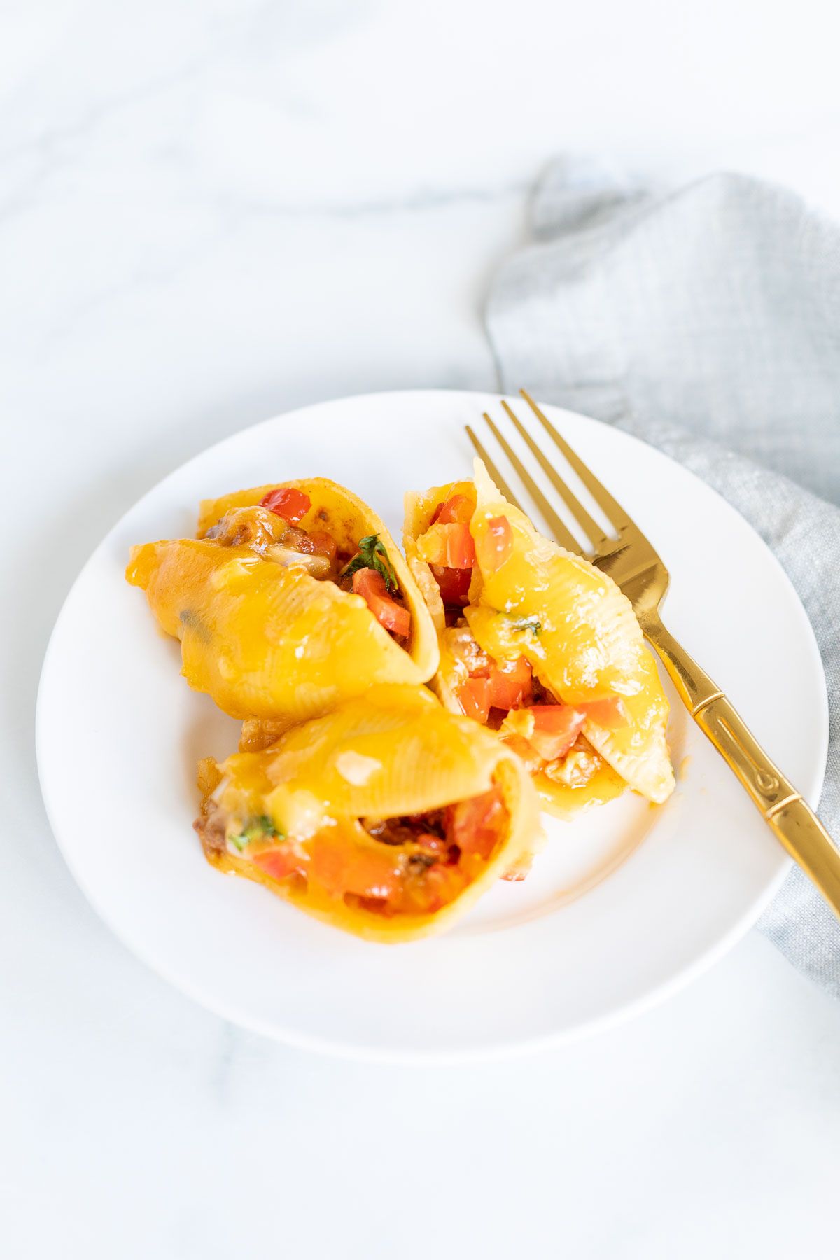 A serving of taco stuffed shells on a white plate with a gold fork.