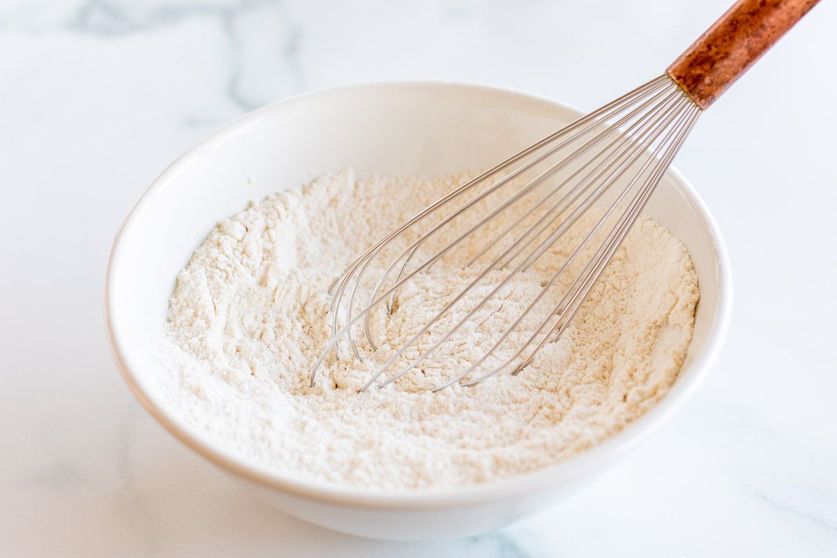 Flour and dry baking ingredients being whisked in a white mixing bowl.
