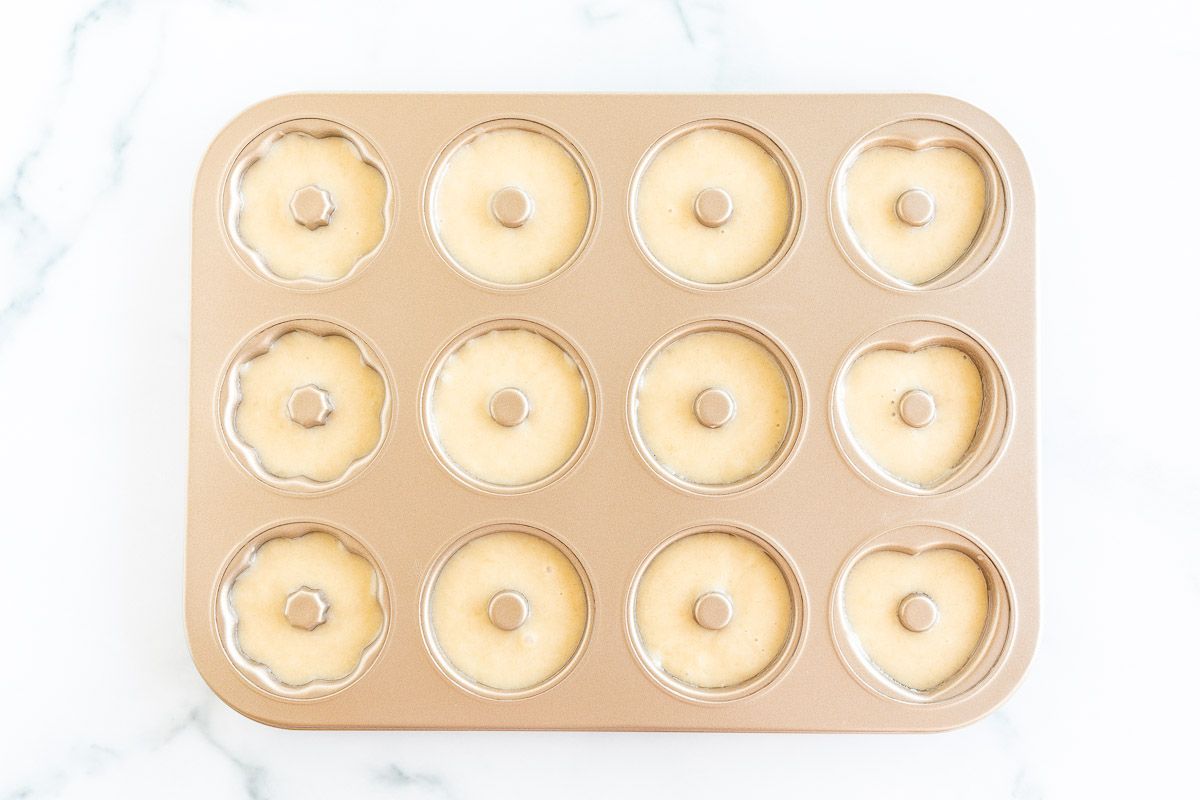 A gold donut pan with batter inside each cavity.