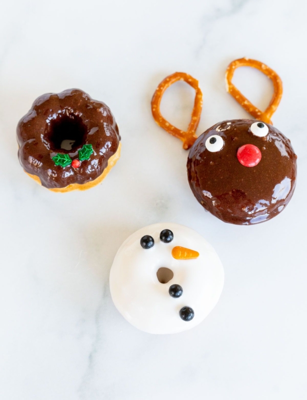 Three cute Christmas donuts on a marble countertop.