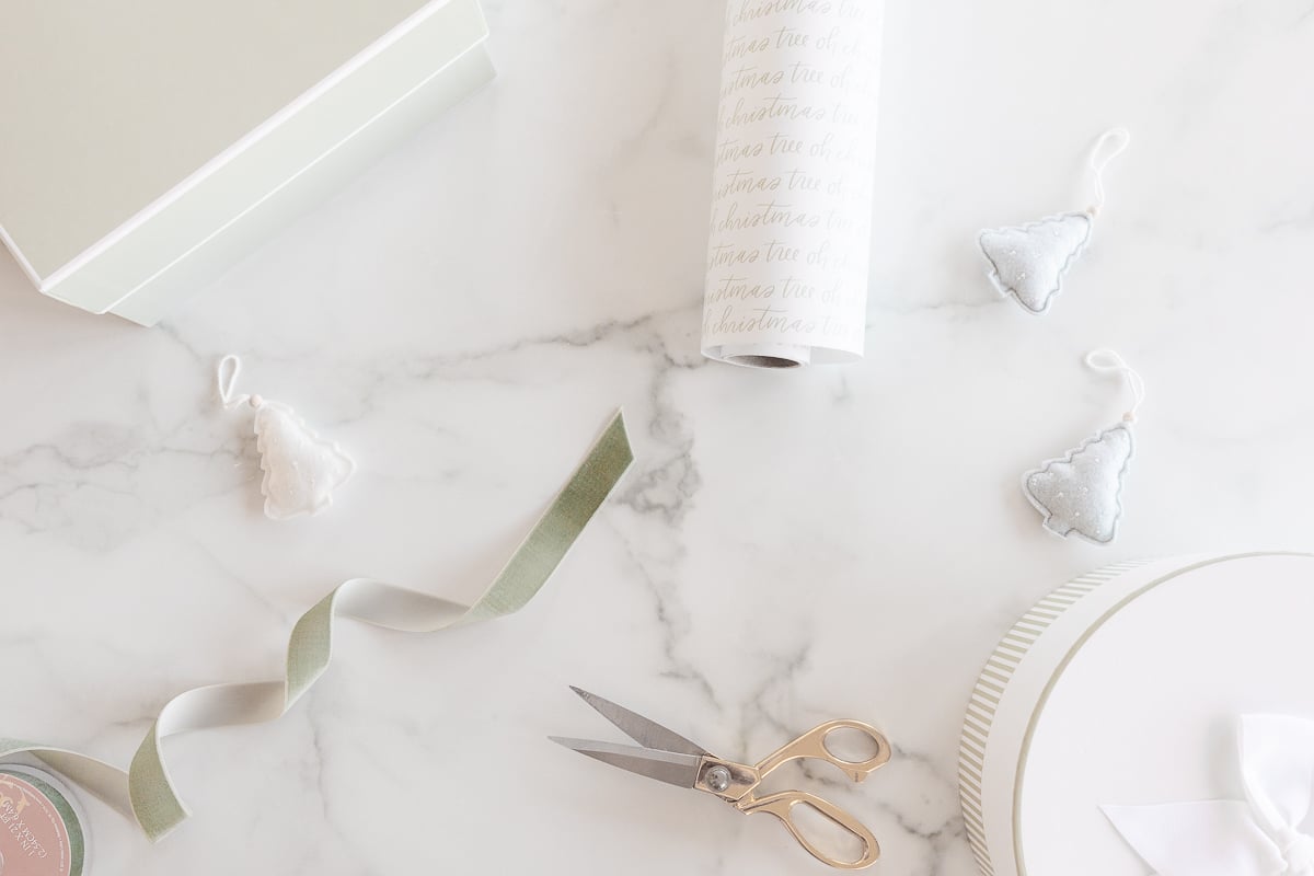 Gift ideas arranged on a marble table, featuring a white box adorned with a ribbon and scissors.