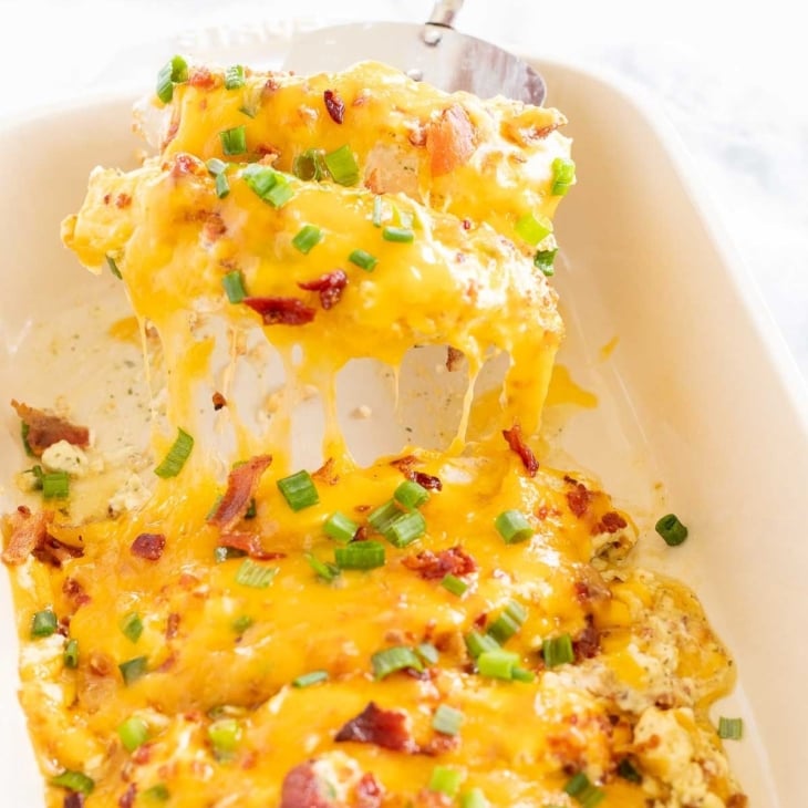 Baked crack chicken breasts in a white baking dish, with a silver spatula lifting a serving out.
