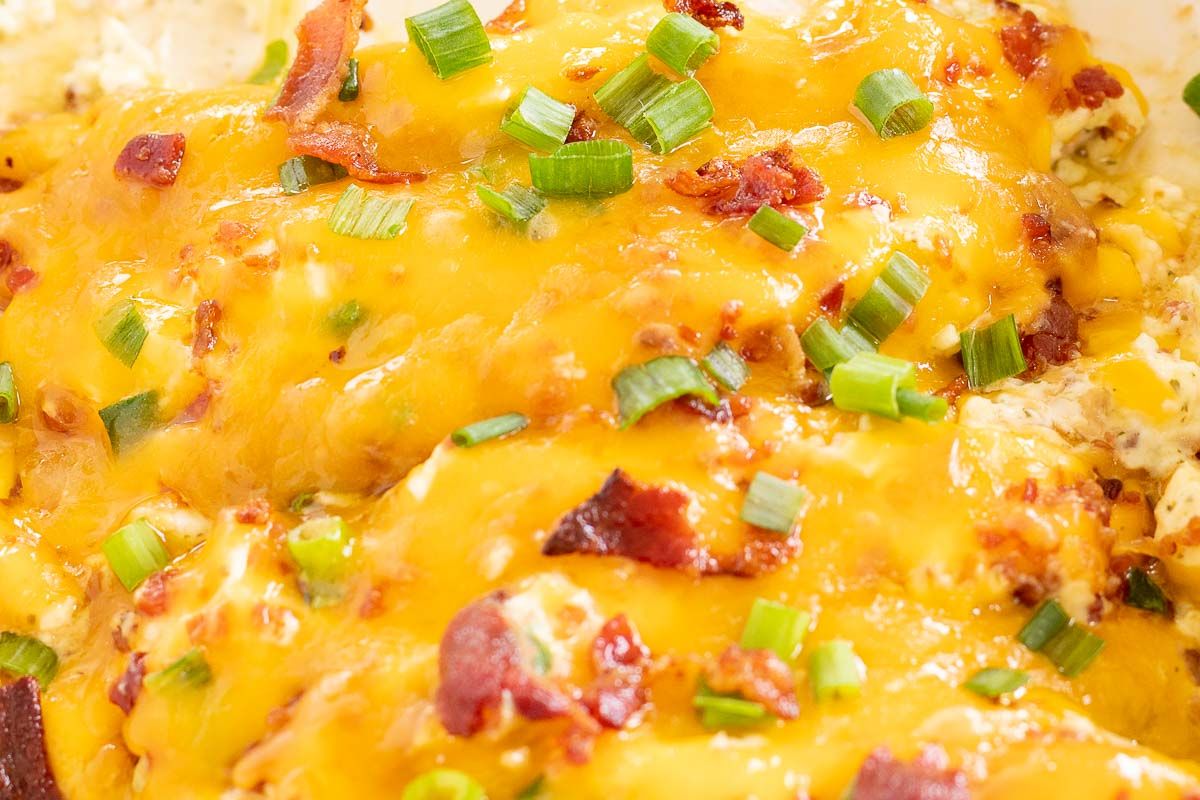 A close up of cheesy crack chicken breasts, topped with green onions and bacon