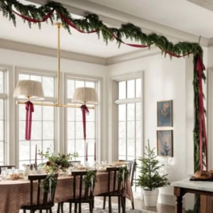 Dining room decorated for the holidays with cedar garland and red ribbons, a set dining table, and a small Christmas tree by the window.