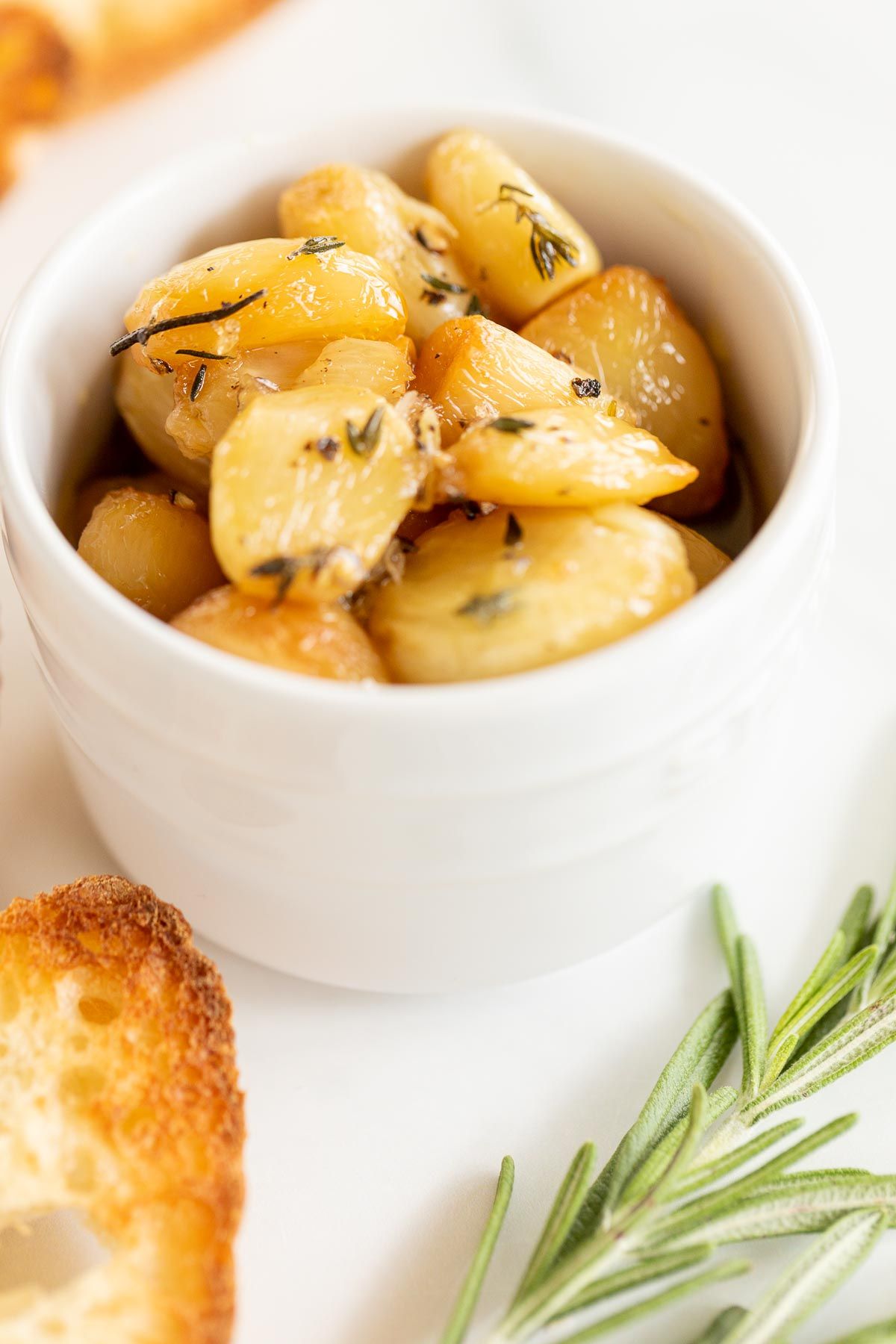 A white bowl full of garlic confit surrounded by crostini and fresh rosemary TeamJiX