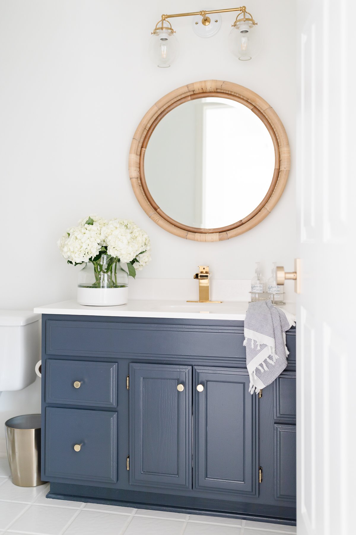 blue vanity rattan mirror double sconce and flowers in bath