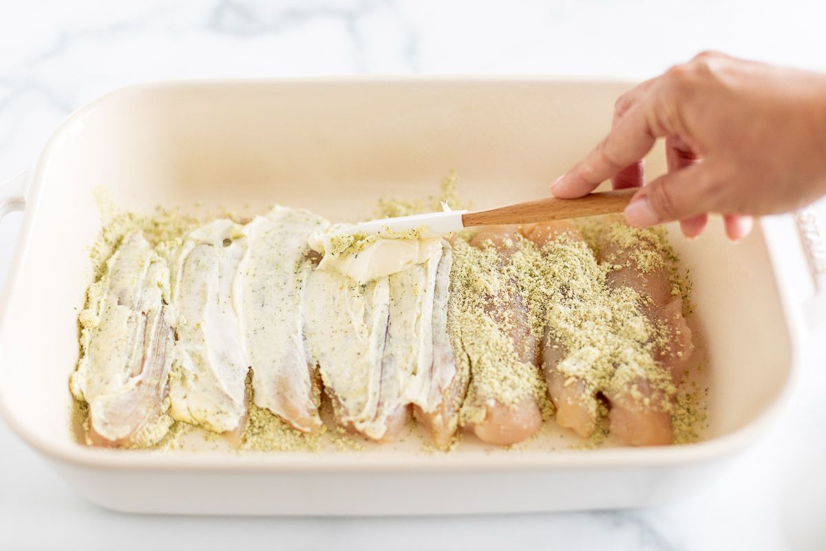Chicken tenderloins topped with seasoning in a white baking dish, prior to baking.