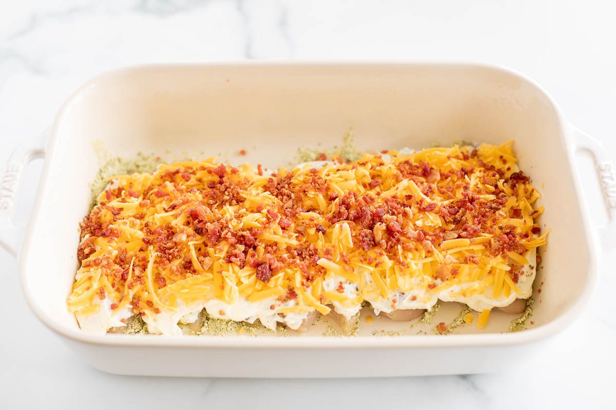 A white baking dish with cheesy crack chicken, topped with green onions and chopped bacon.