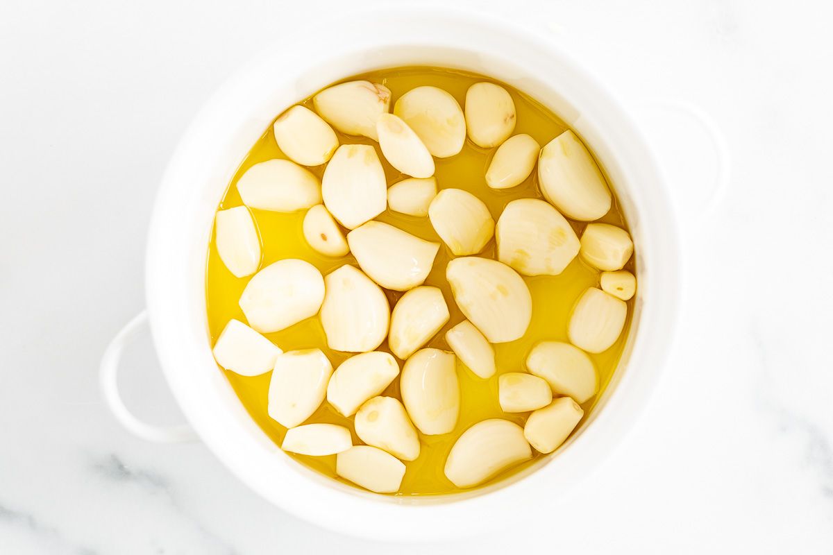 A white bowl full of garlic cloves and olive oil.