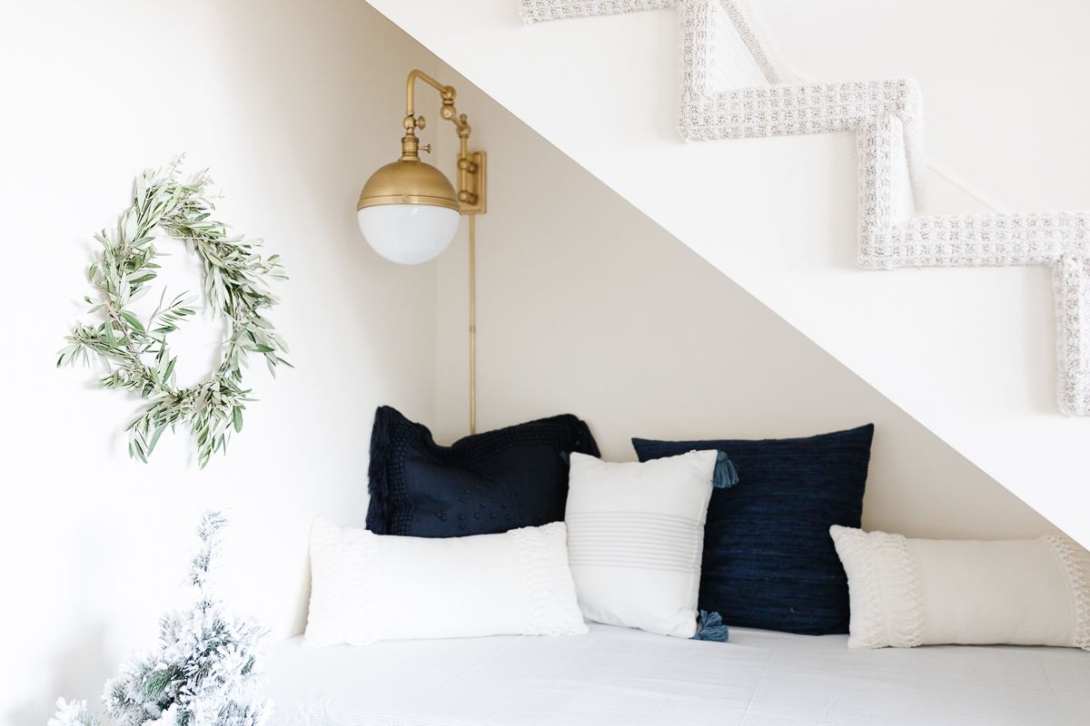 A fresh Christmas wreath replaces wall art in a blue and white reading nook under a staircase. 