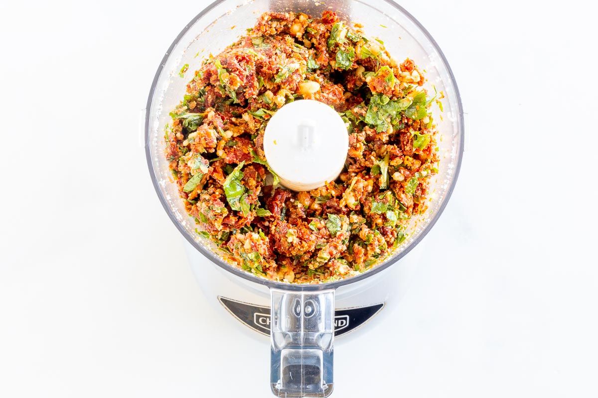 A food processor filled with ingredients for sun dried tomato pesto