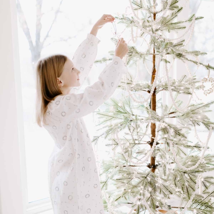 a little girl decorating a sparse christmas tree for a minimalist christmas