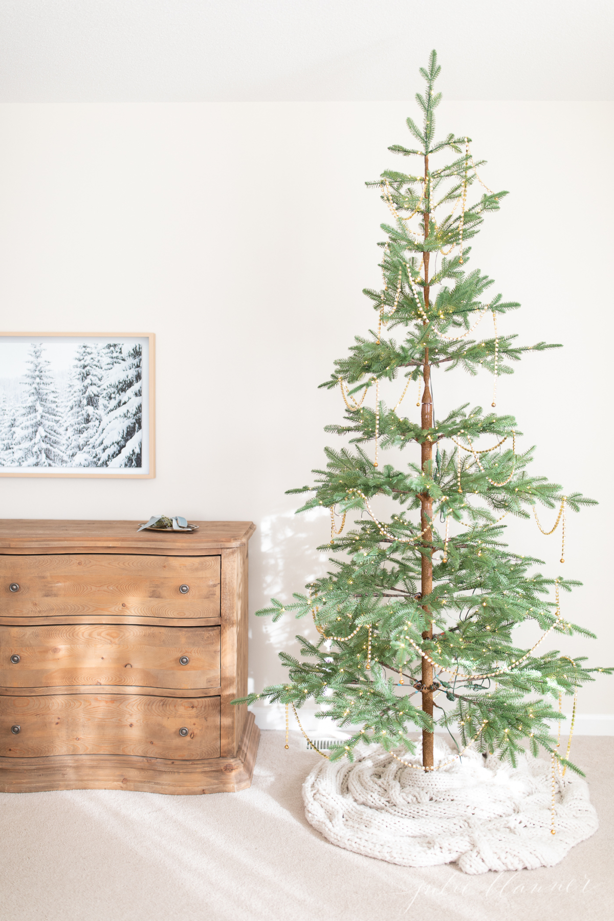 A sparse Christmas tree stands in a room alongside a dresser.