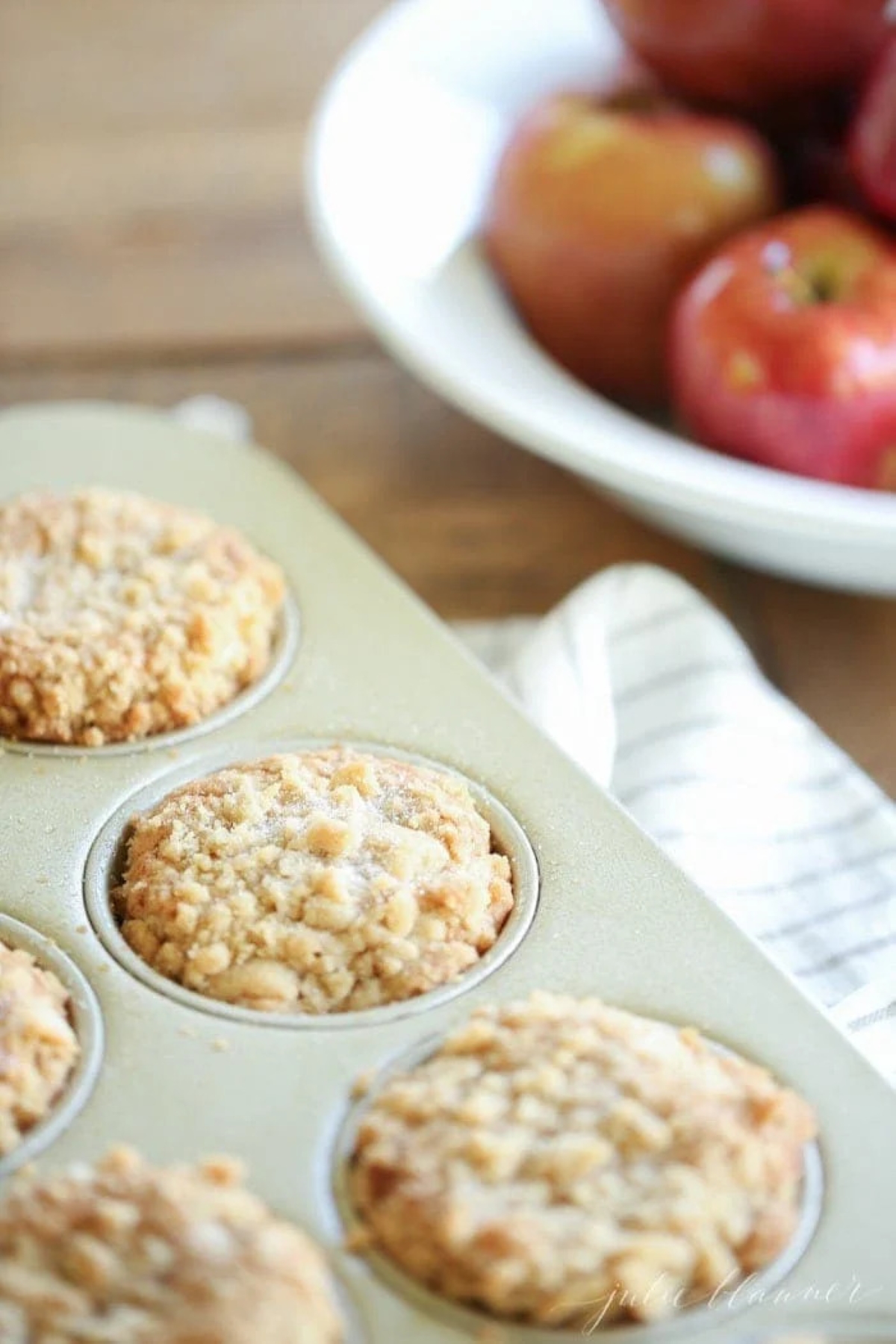 apple cobbler muffins in a gold muffin pan, bowl of red apples in the background