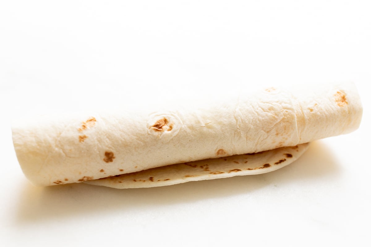 A tortilla, rolled on a white surface.