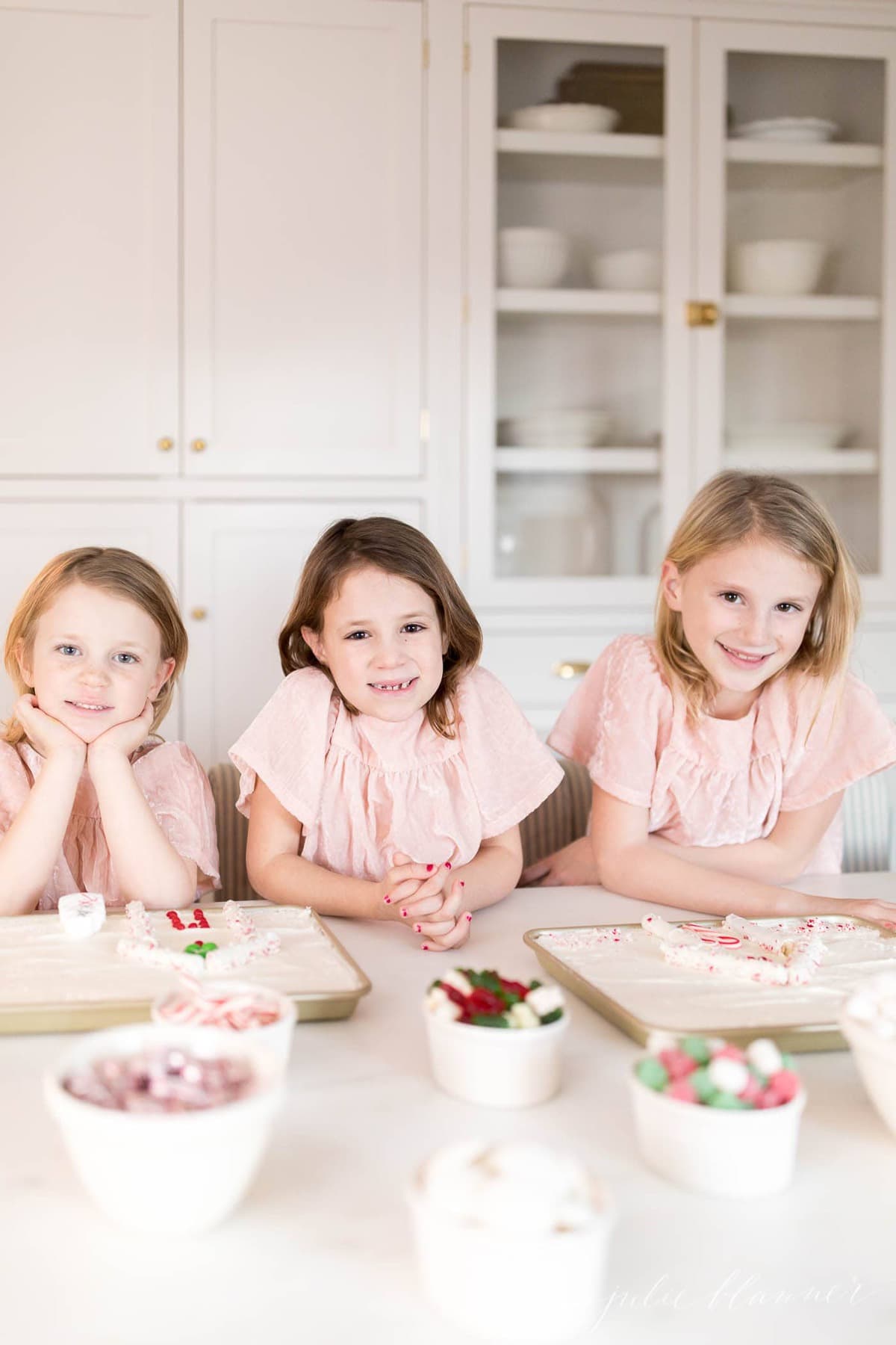 Three little girls in front of Christmas sugar cookie cakes. 