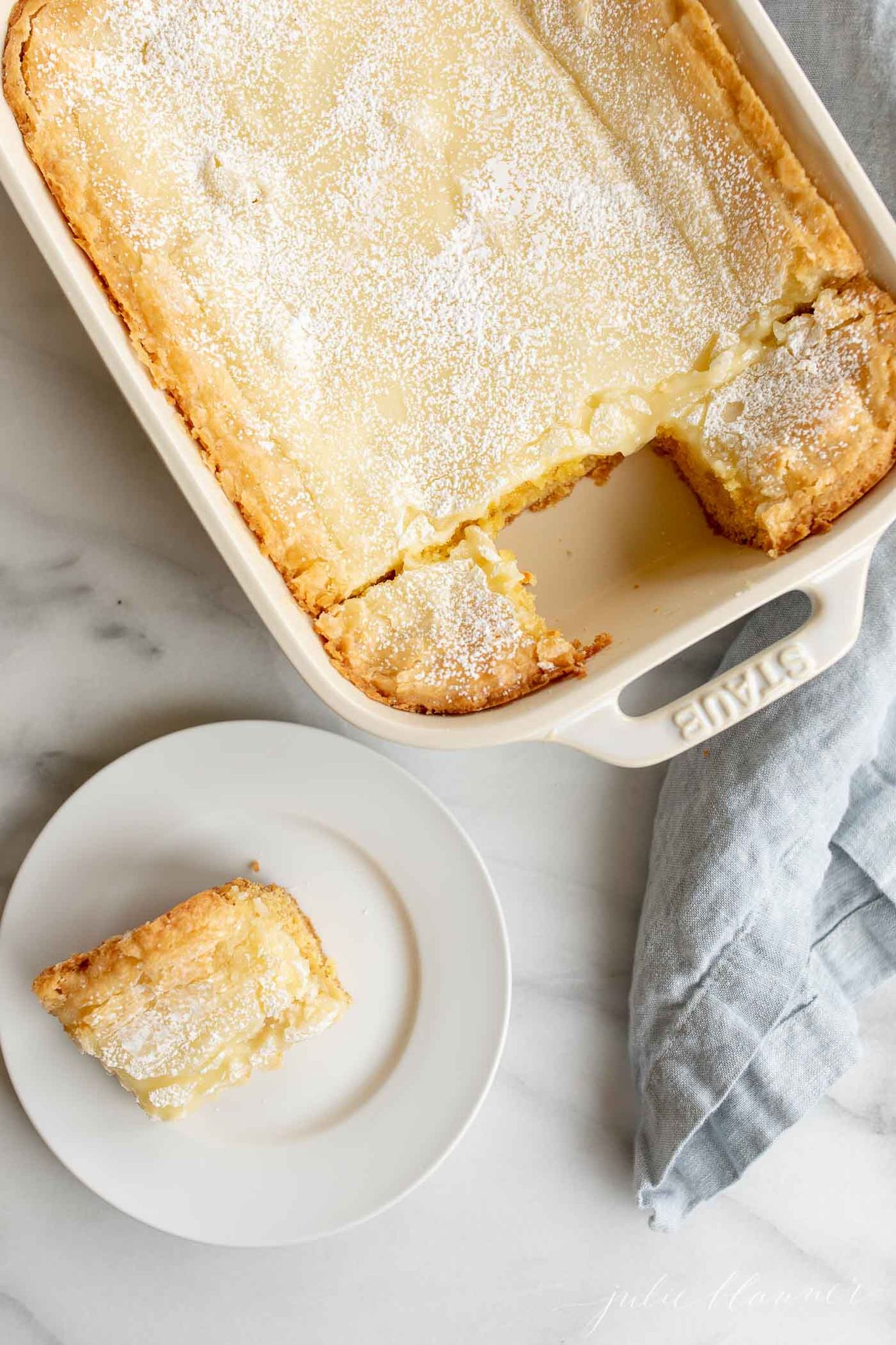 gooey butter cake in a white ceramic baking dish, with a slice removed onto a white plate. 
